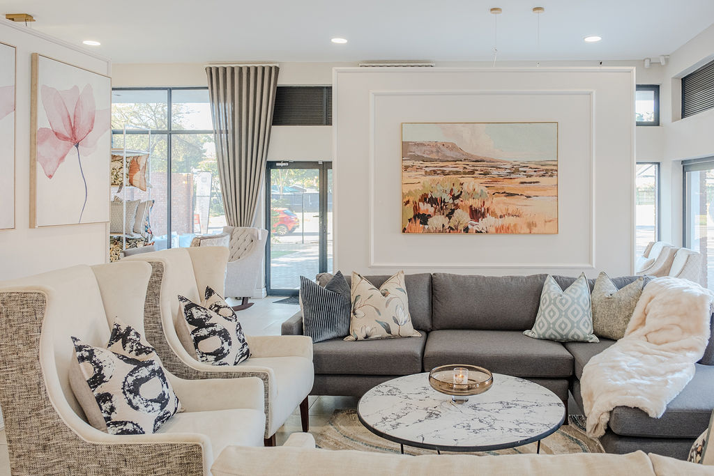 Grey sectional and wingback chairs with landscape art in a sunlit living room